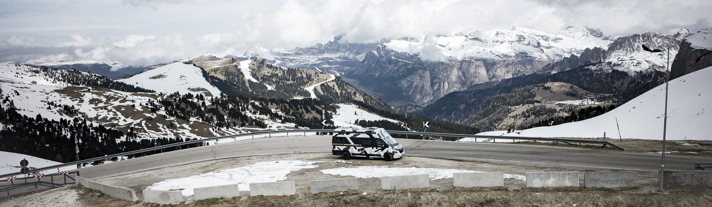 Camper auf einer Passstraße vor verschneiten Alpengipfeln